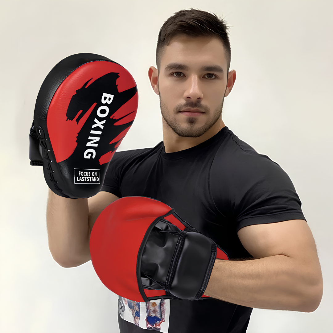 Man with red and black boxing mitts, demonstrating their use in training, ideal for combat sports such as boxing or Muay Thai.